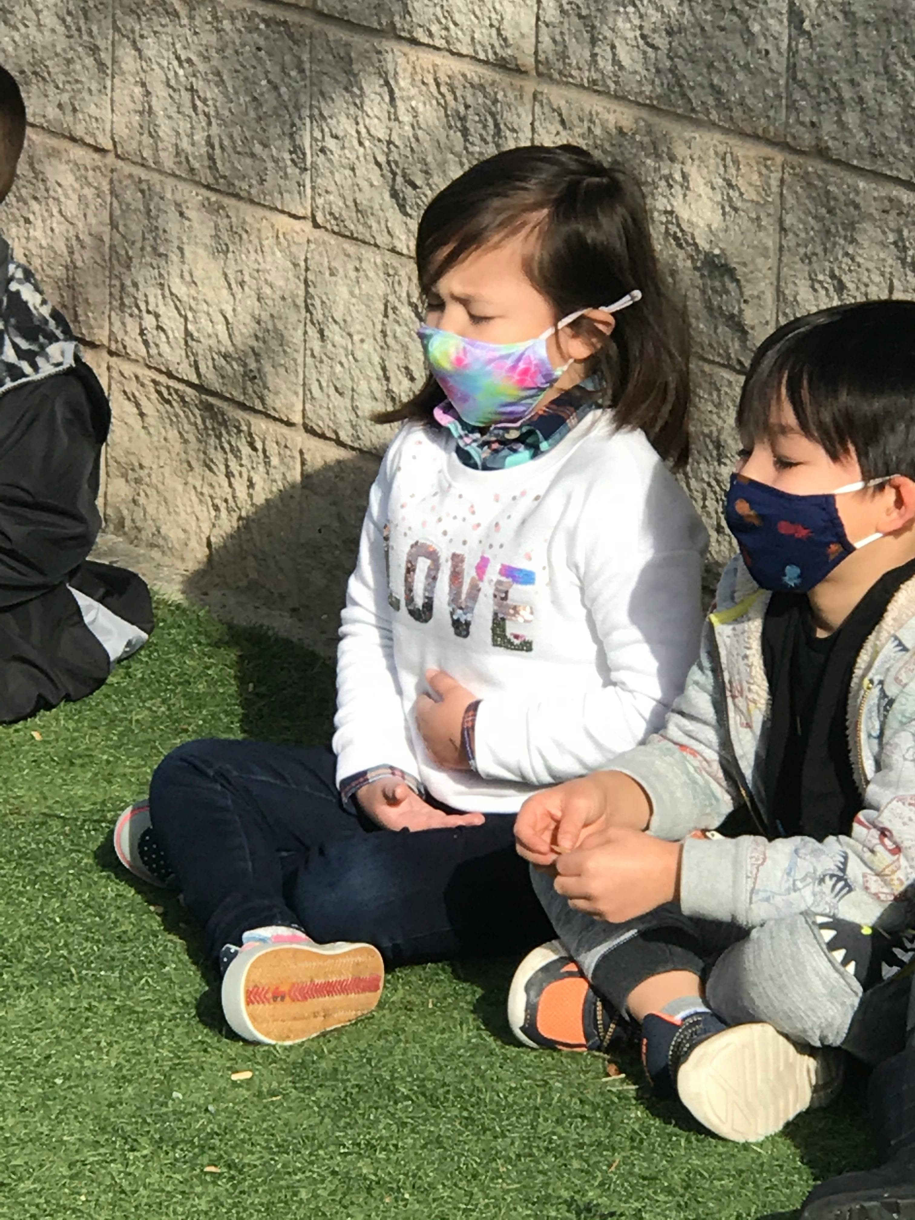 Two children wearing face masks sitting on grass