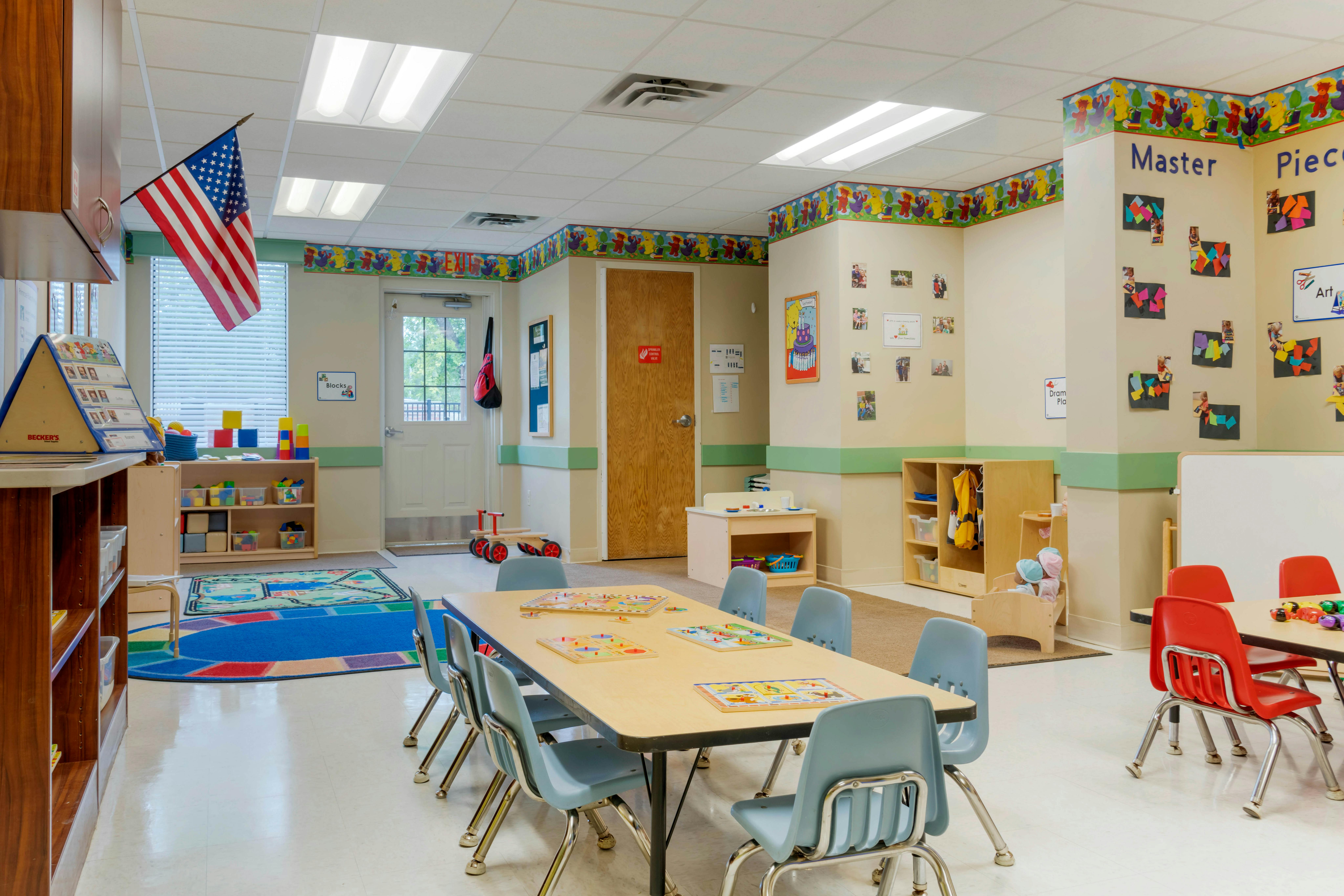A colorful classroom with small tables and chairs, toys, and an American flag hanging