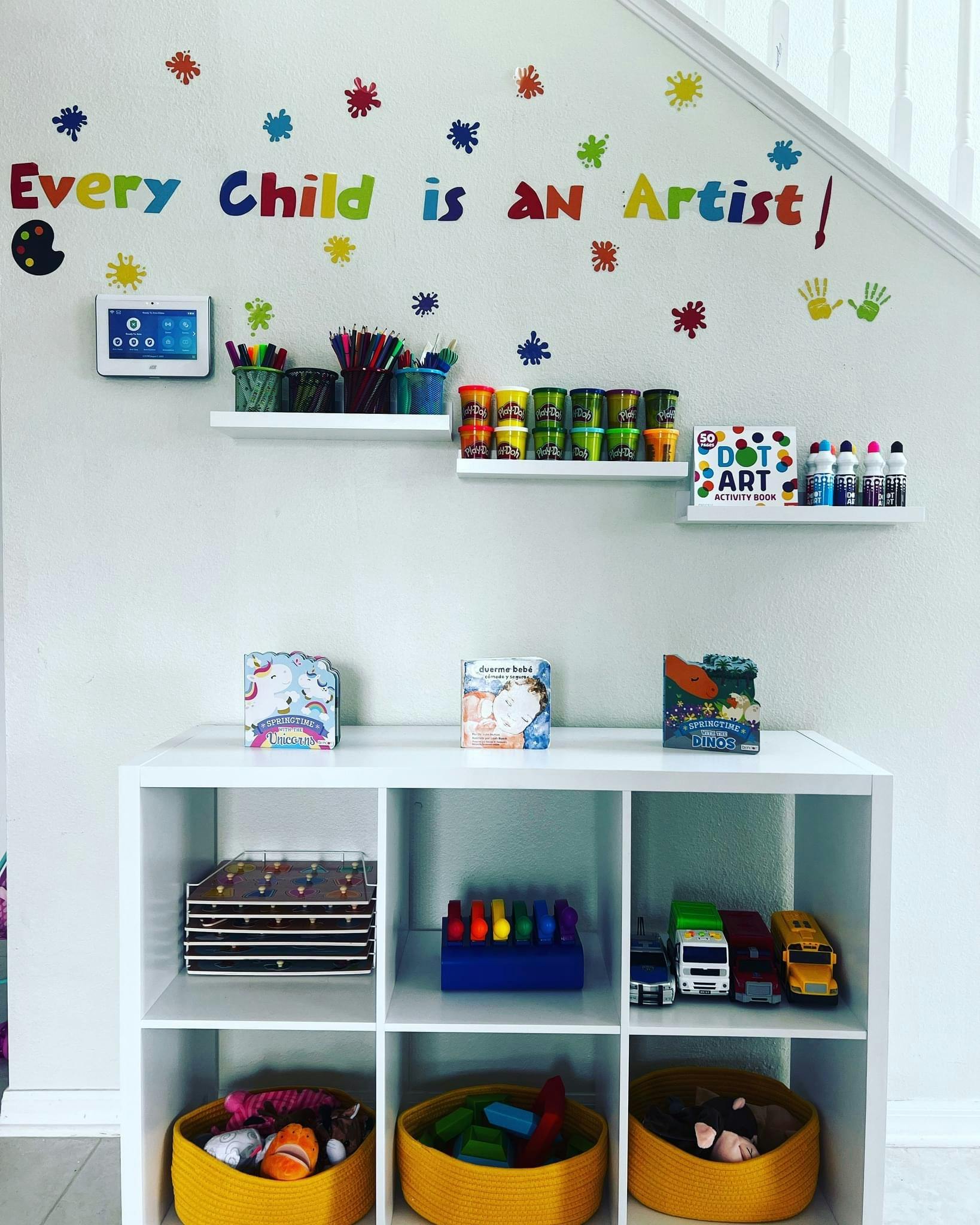 Art supplies and toys on shelves with "Every Child is an Artist" on the wall