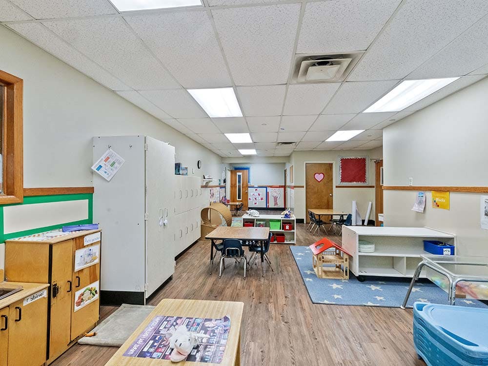 Empty preschool classroom with small tables, chairs, and cubbies