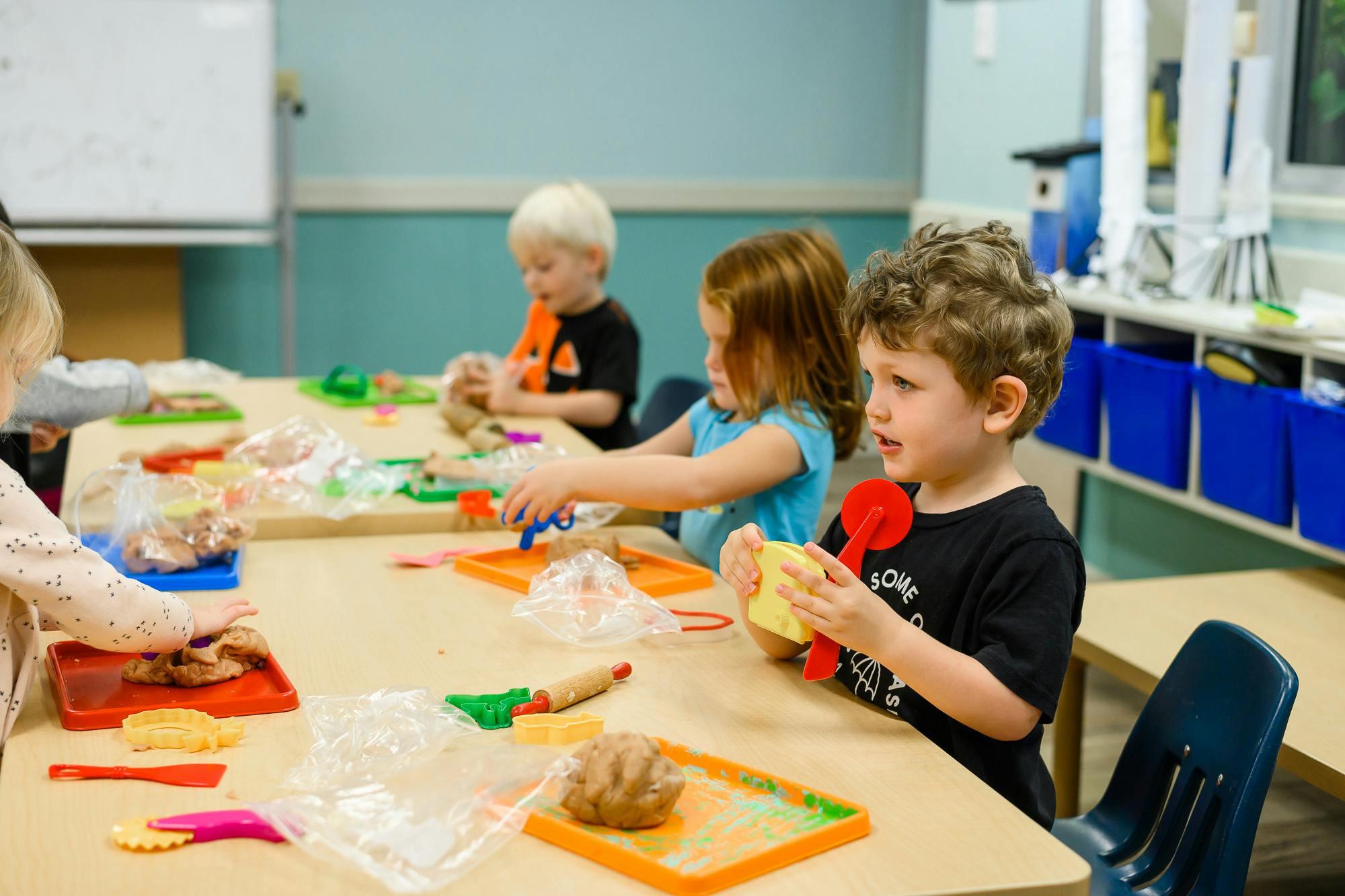 Children playing with modeling clay at a table in a classroom