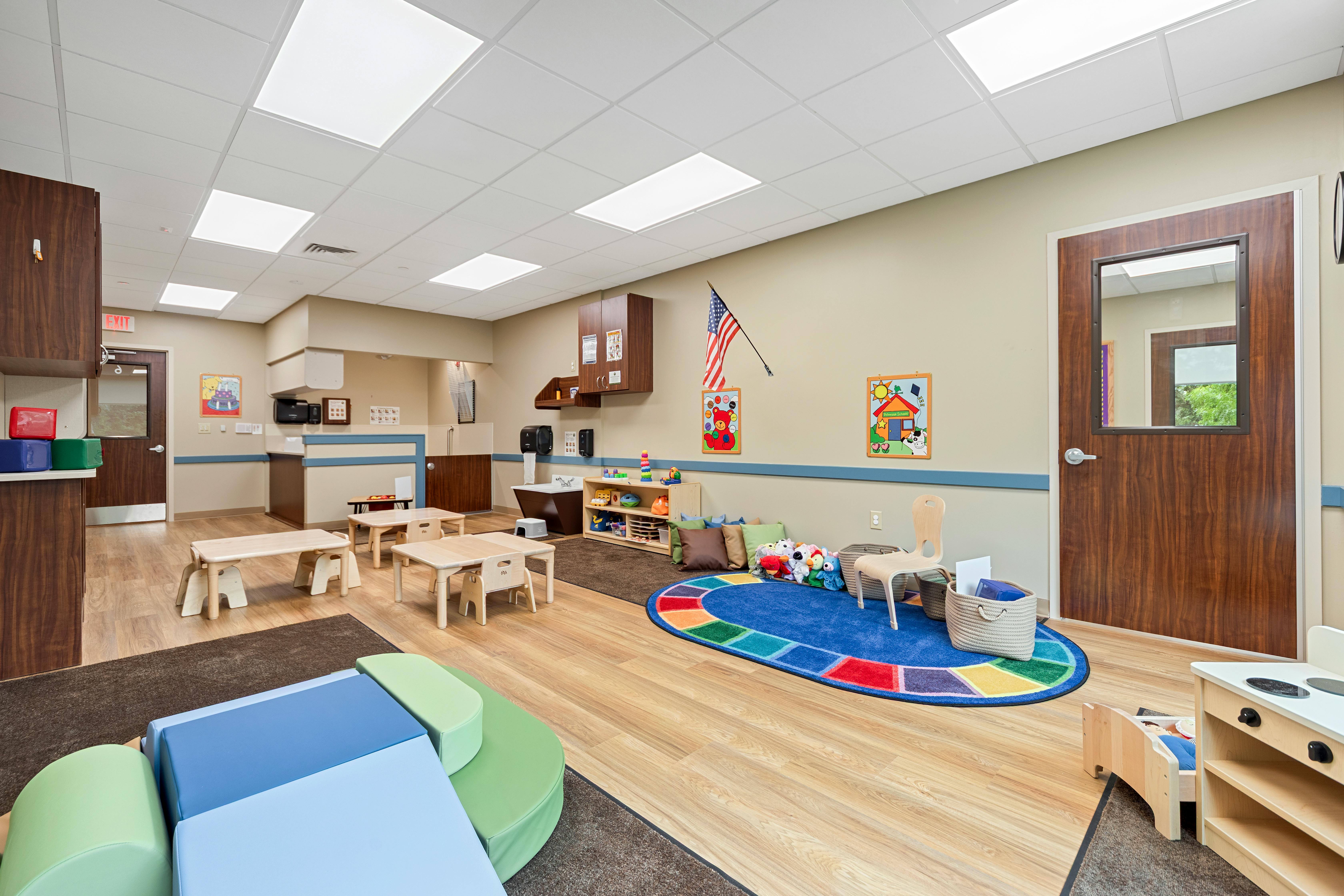 An empty childcare classroom with small tables, chairs, and play areas
