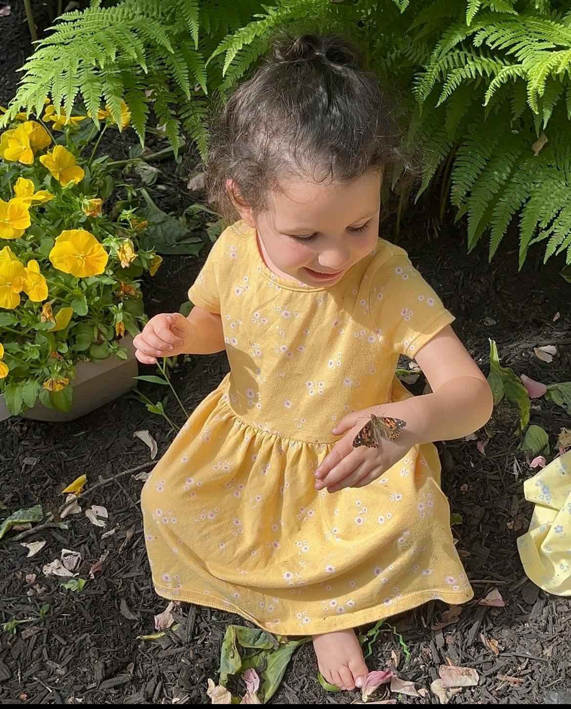 Child sitting in a garden with a butterfly resting on their hand
