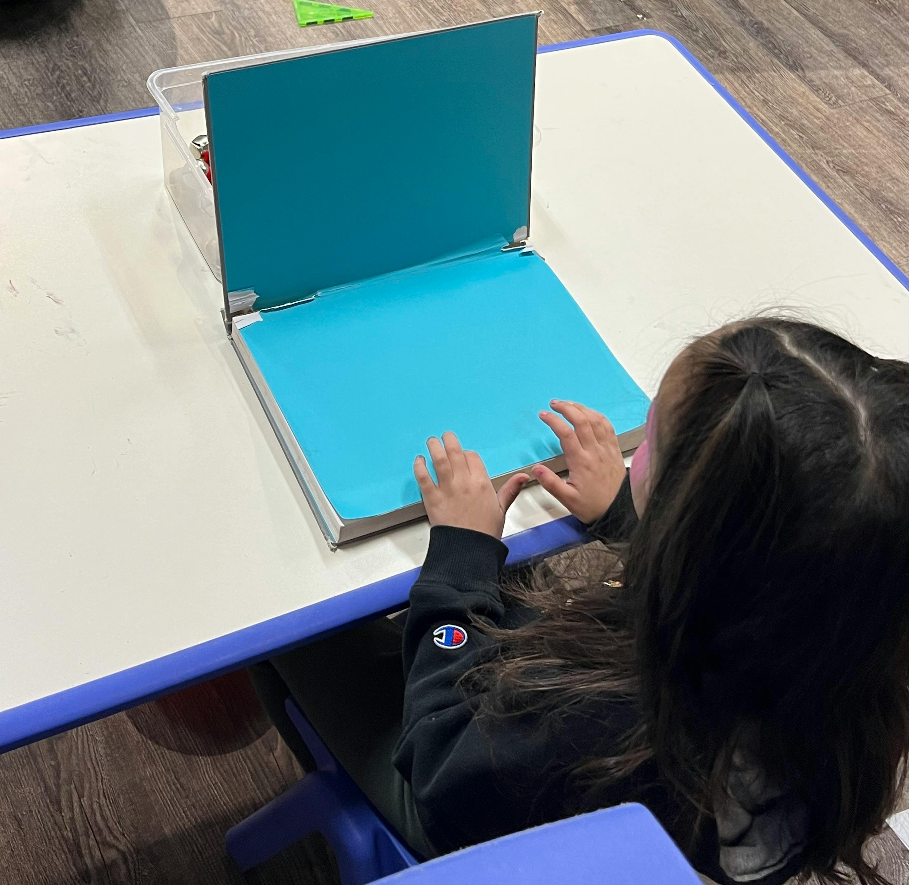 Child sitting at a table with hands on a blue folder