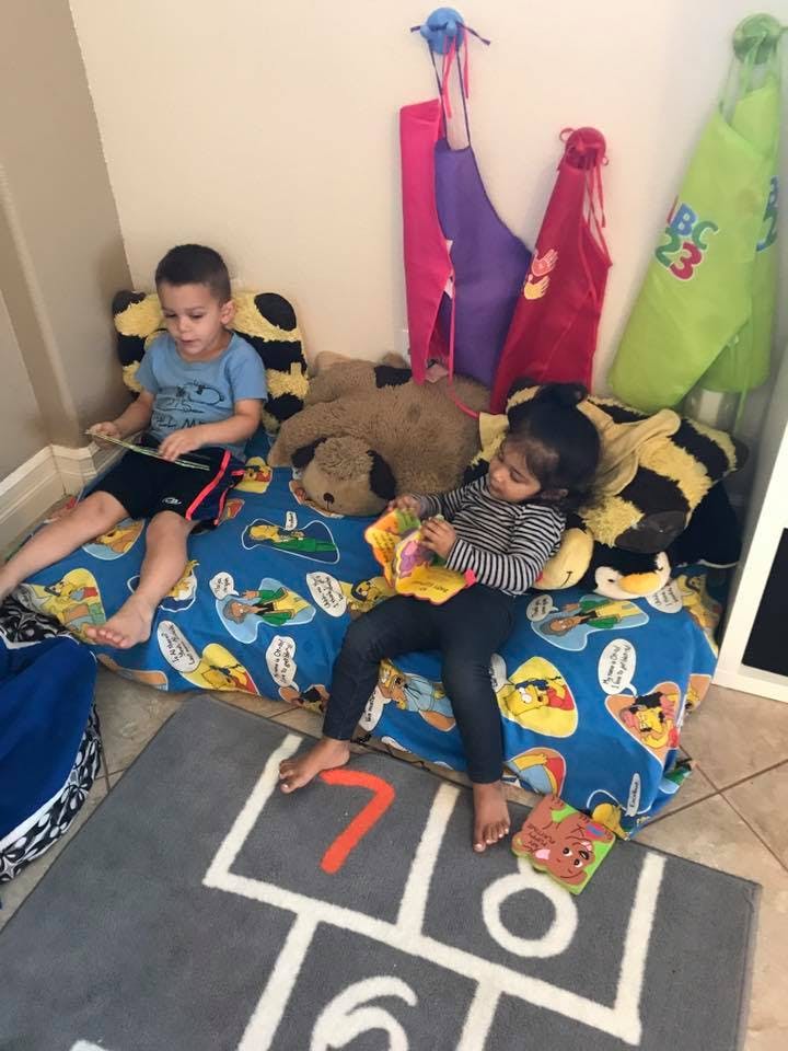 Two children sitting on a blue cushion with stuffed animals