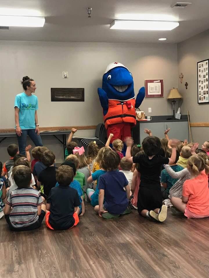 Person and mascot interacting with children sitting on the floor