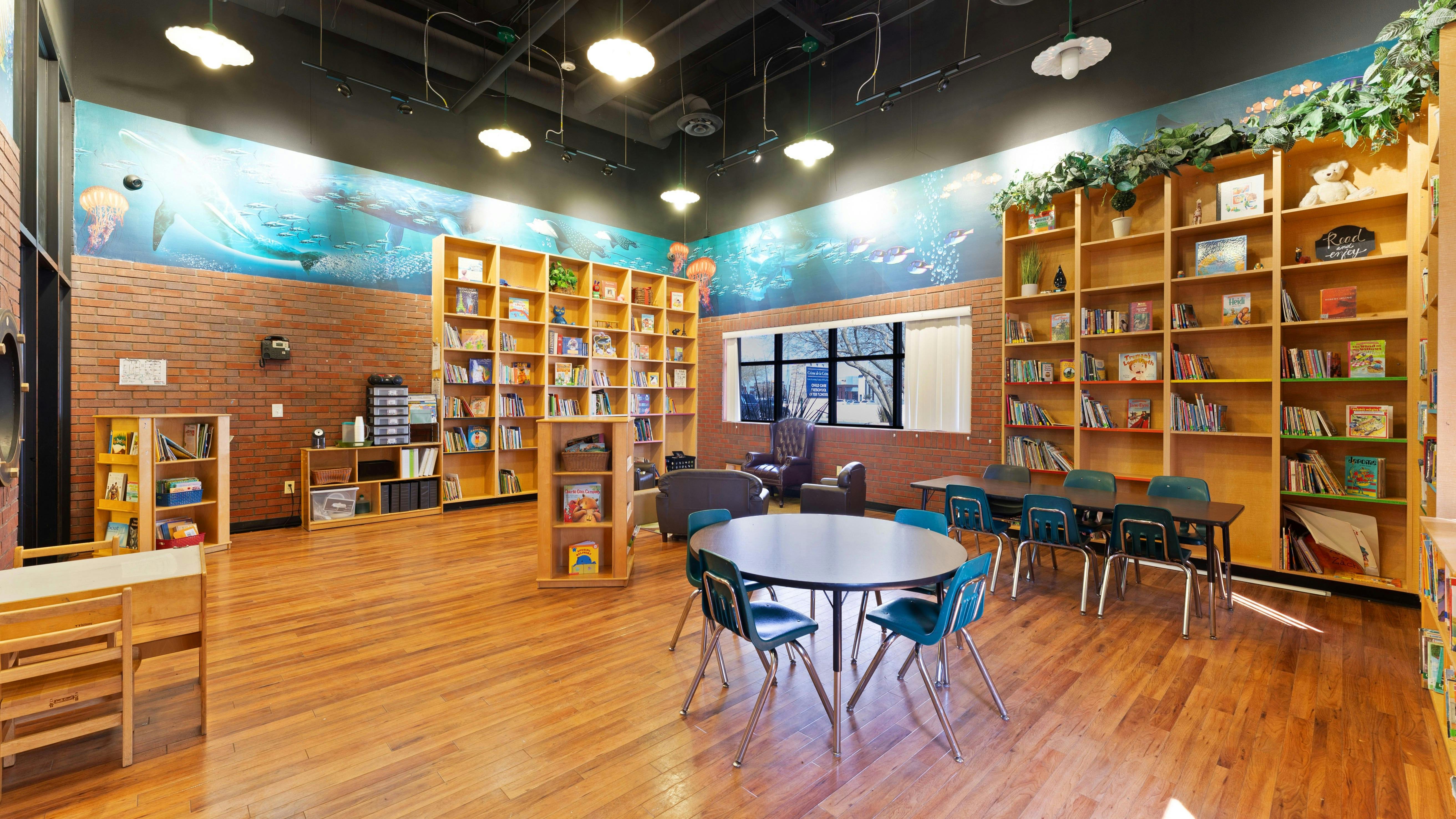 Classroom or library with wood floors, bookshelves, small tables, and ocean-themed mural