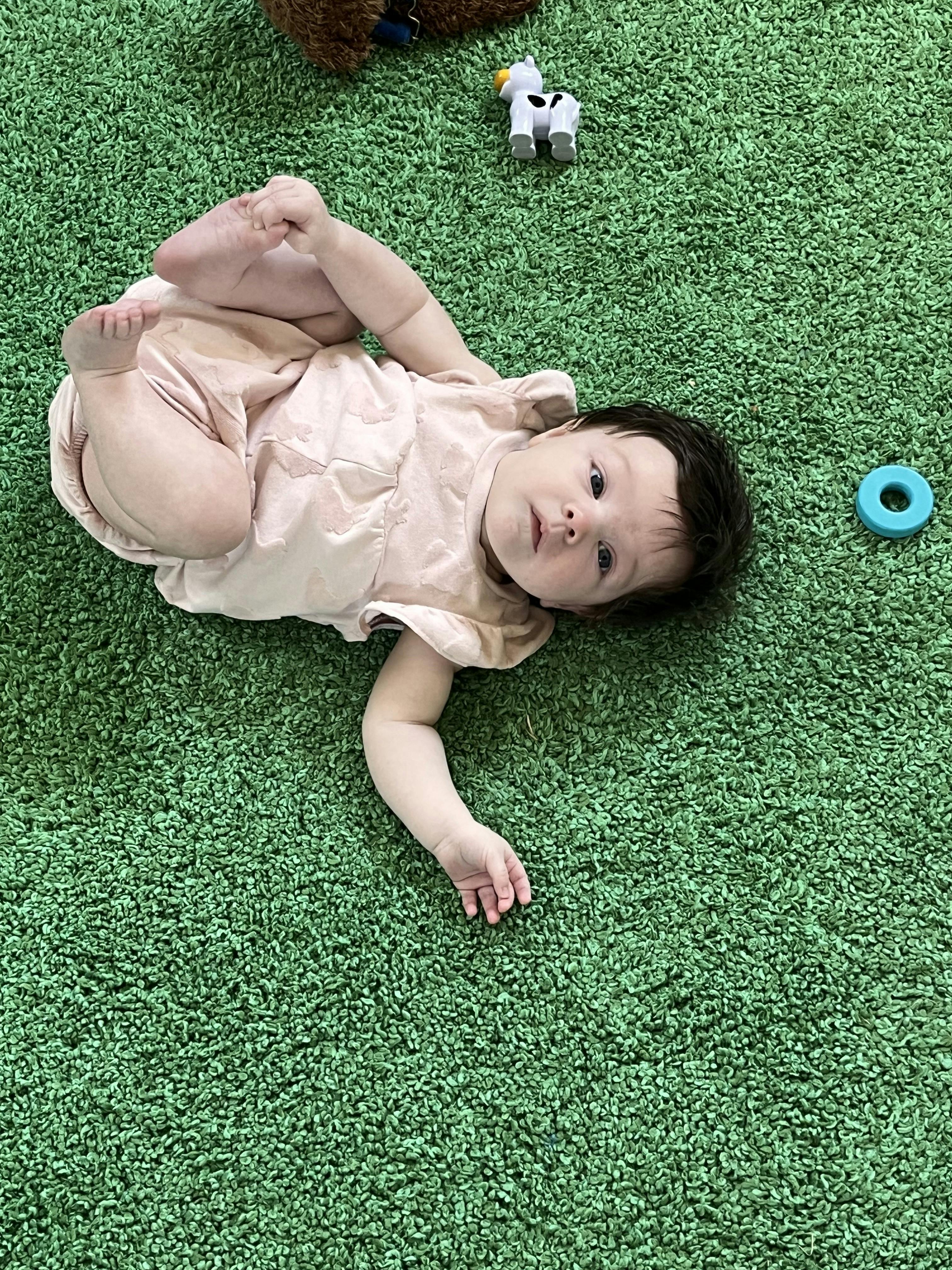 Child lying on a green rug holding their feet