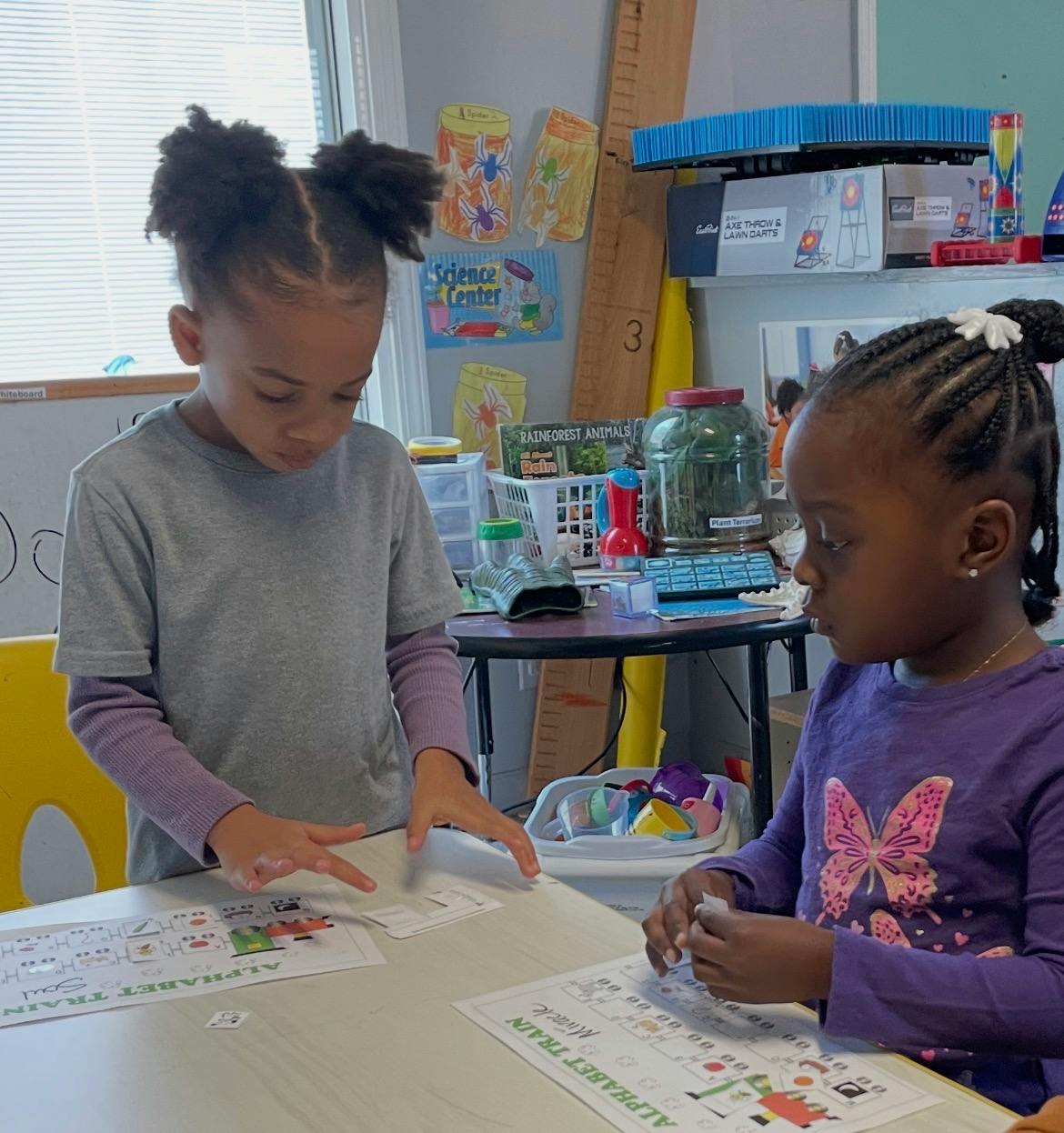 Two children playing with alphabet train cards at a table in a classroom