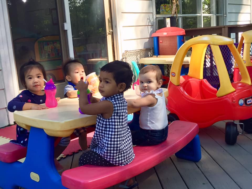 Four children sitting at a small picnic table outdoors