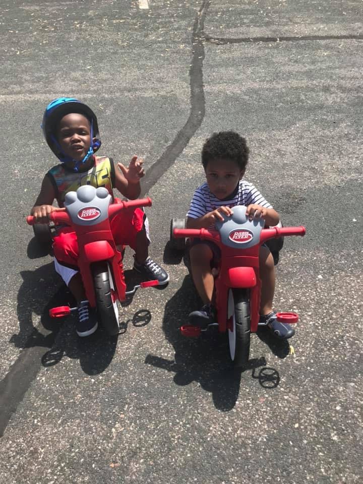Two children riding red tricycles on pavement