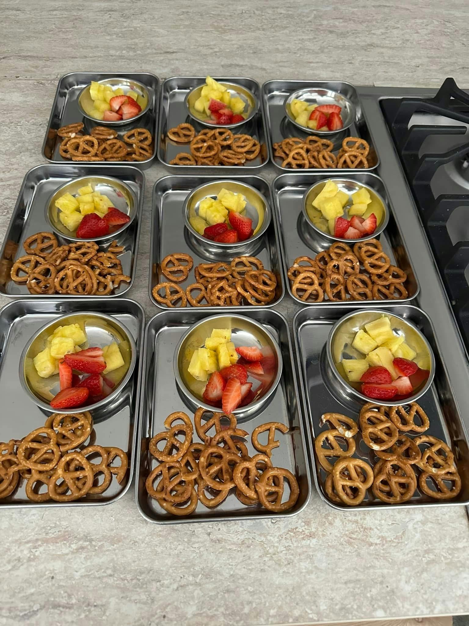 Several metal trays each containing pretzels and a bowl of pineapple and berries
