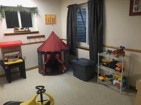 Playroom with a red tent, toy shelf, and ride-on toy