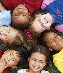 Six children lying in a circle on grass, looking up