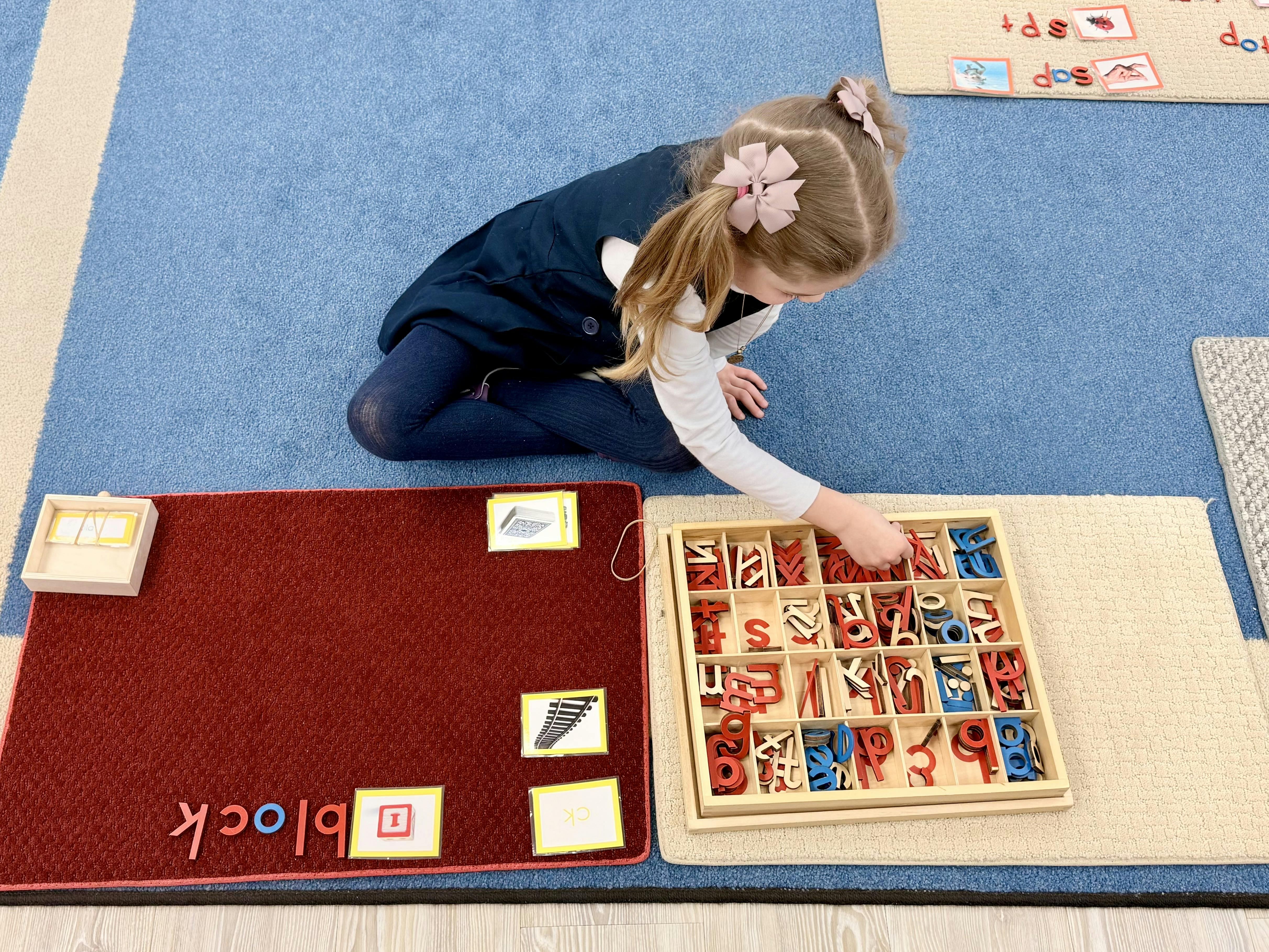 Child on floor selecting letters from a tray during a spelling lesson
