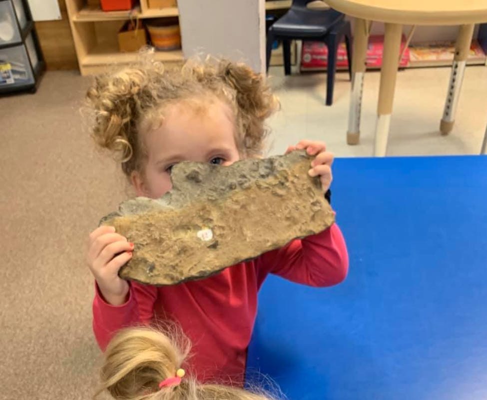Child holding a rock in front of their face