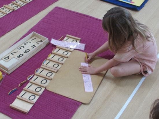 Child writing on paper with number blocks on a mat