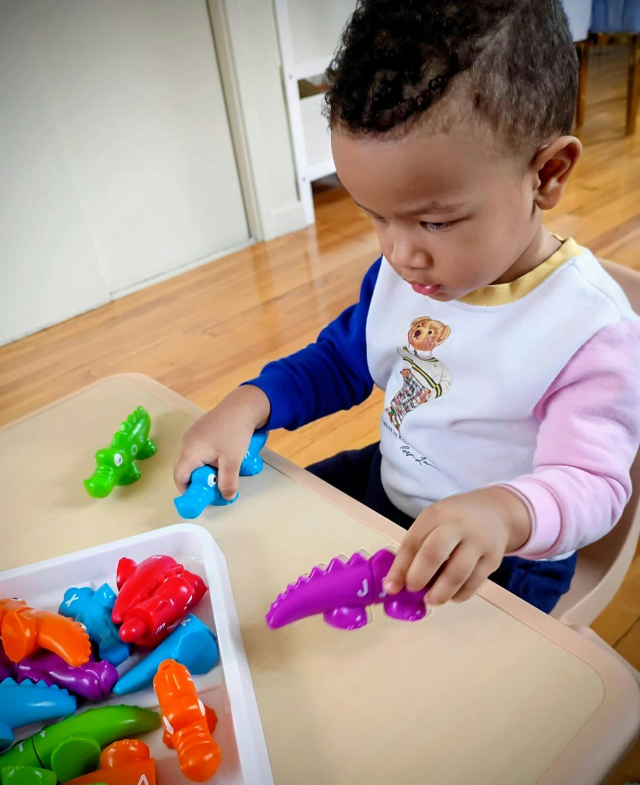 Child playing with colorful crocodile toys on a table