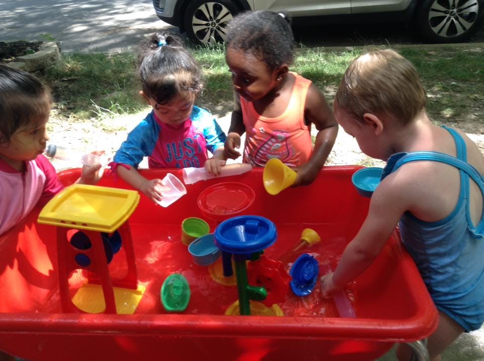 Four children playing with water toys in a red bin