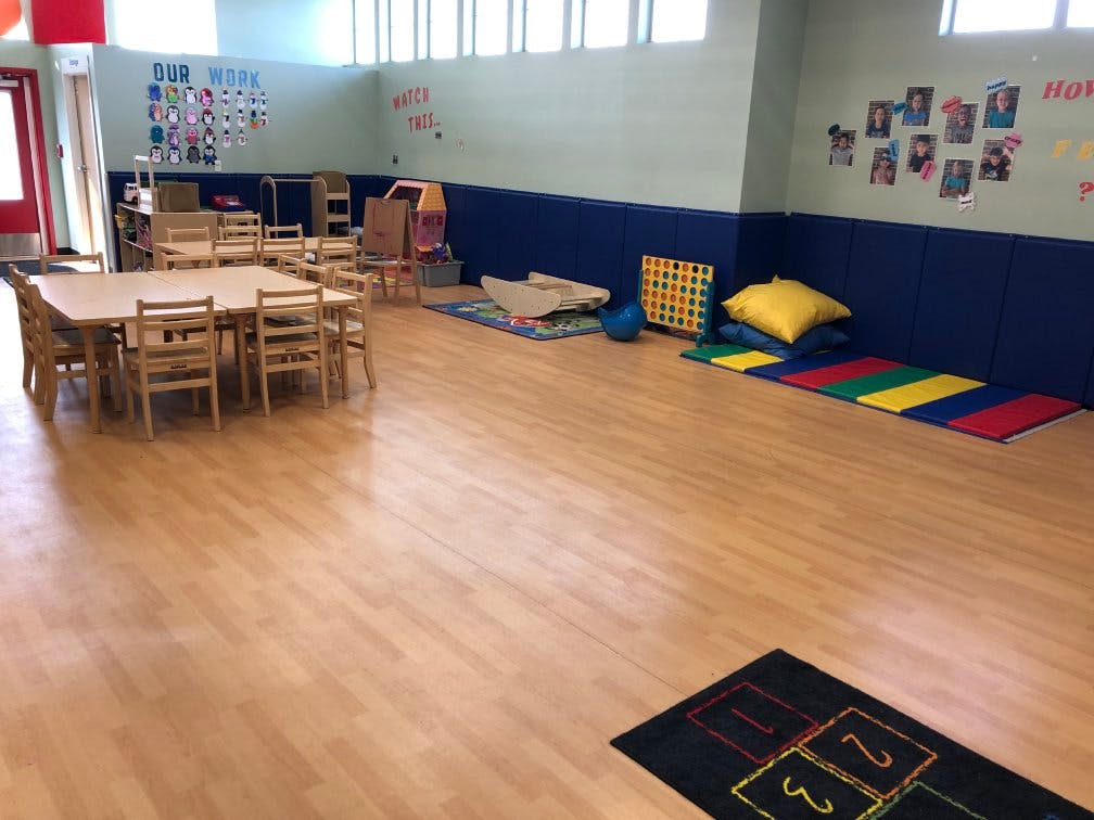 Classroom with tables, chairs, padded wall, mats, and a hopscotch rug