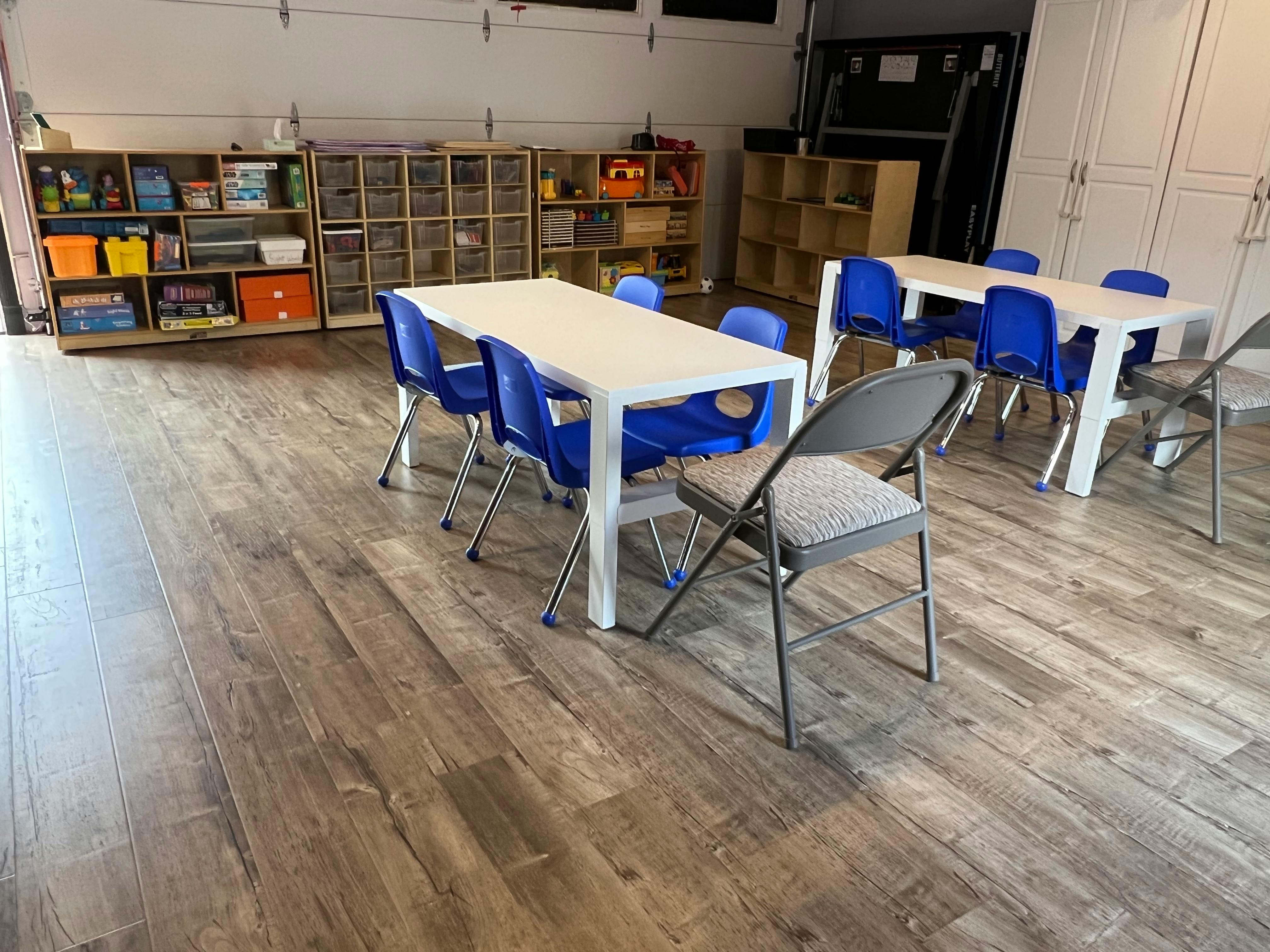 Classroom with white tables, blue chairs, and storage shelves