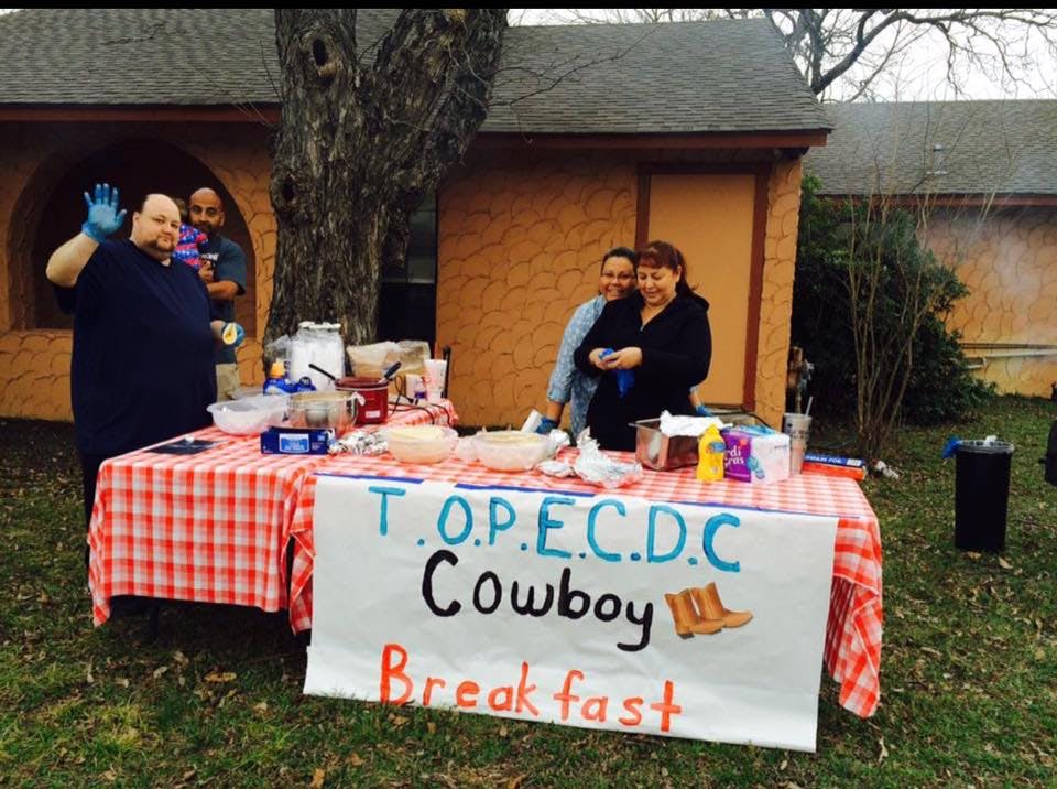 People standing behind a table with a sign that reads "T.O.P.E.C.D.C Cowboy Breakfast"