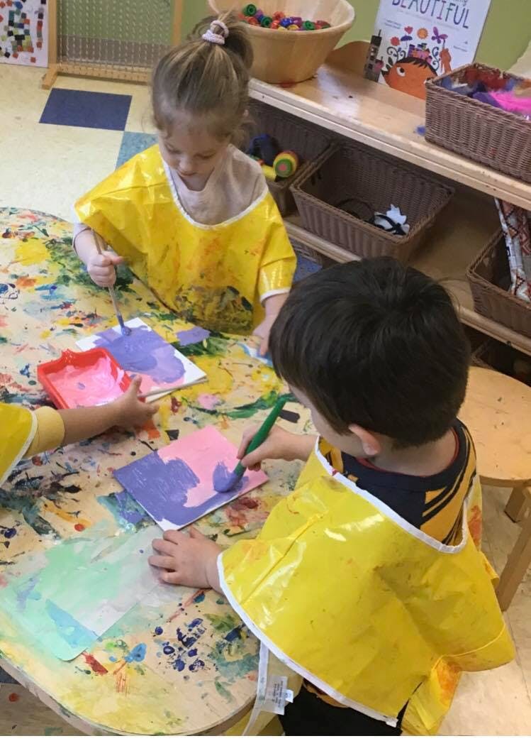 Two children in yellow smocks painting at a table