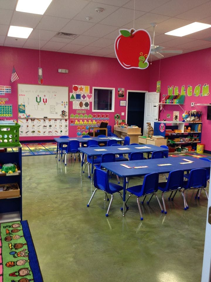 Classroom with pink walls, blue tables and chairs, and a large apple decoration