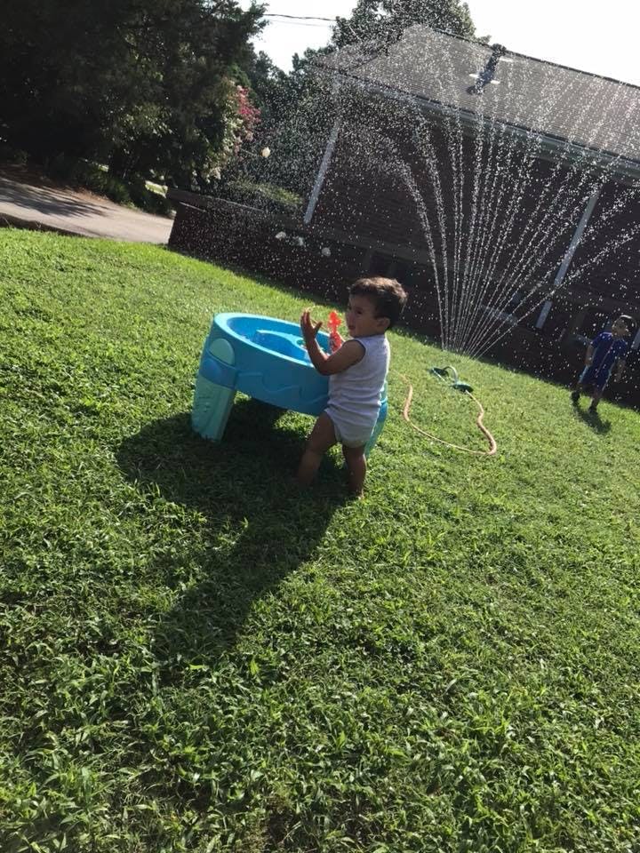 Child playing with a water table in a grassy yard with a sprinkler