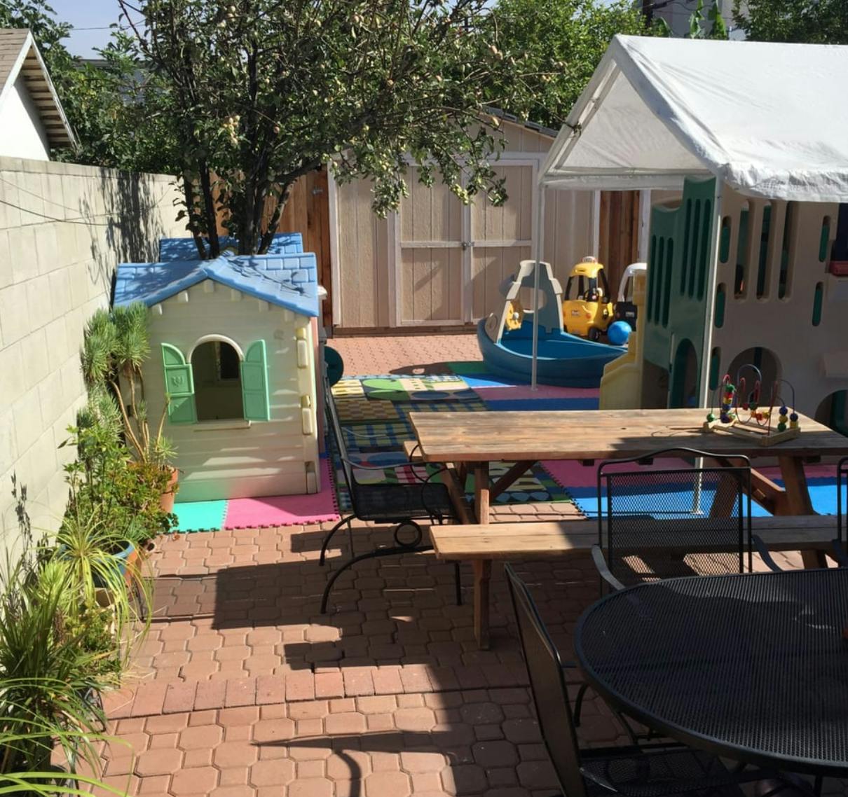 Backyard play area with playhouses, picnic table, and brick patio