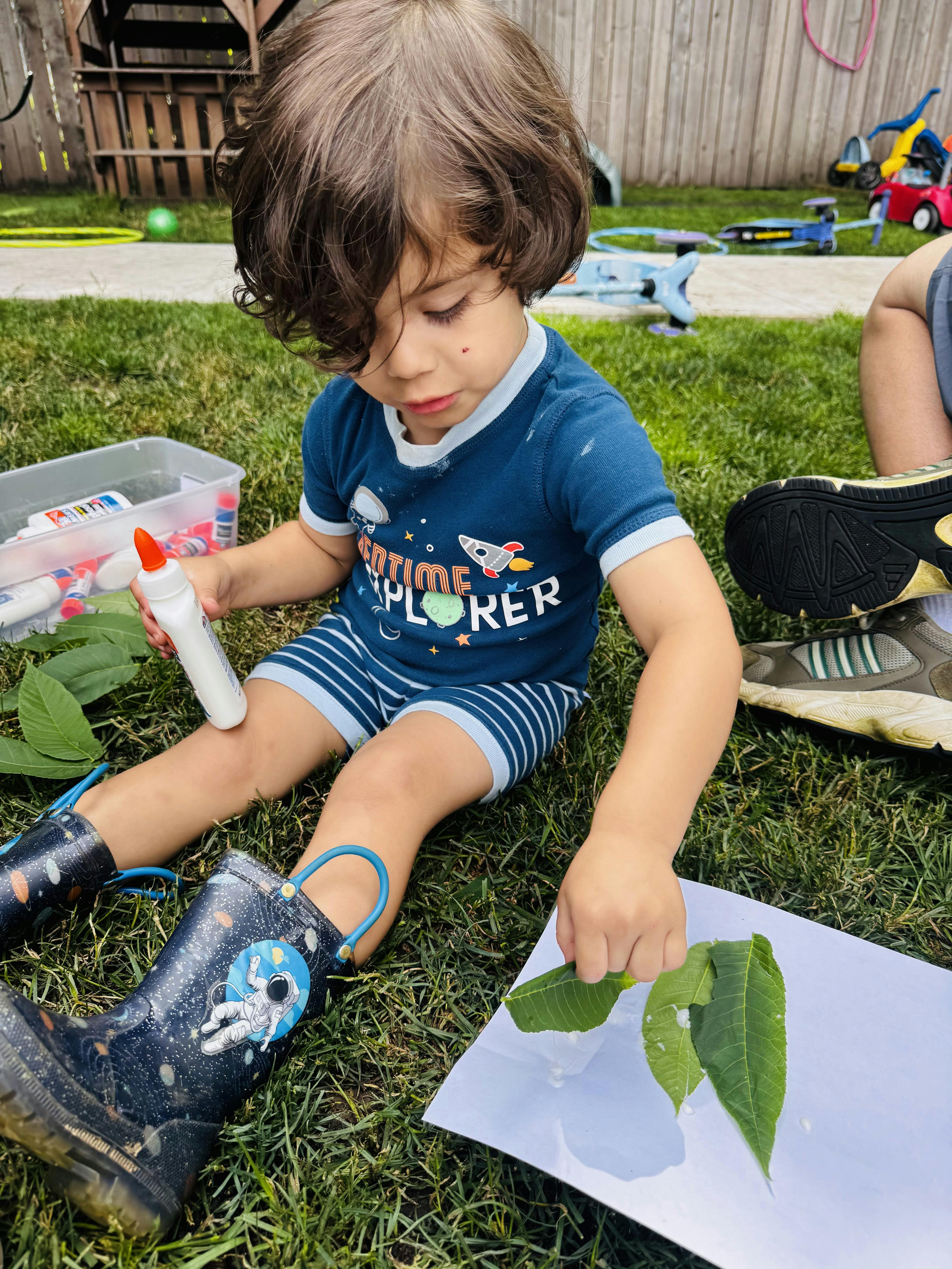 child sitting on grass, gluing leaves to paper
