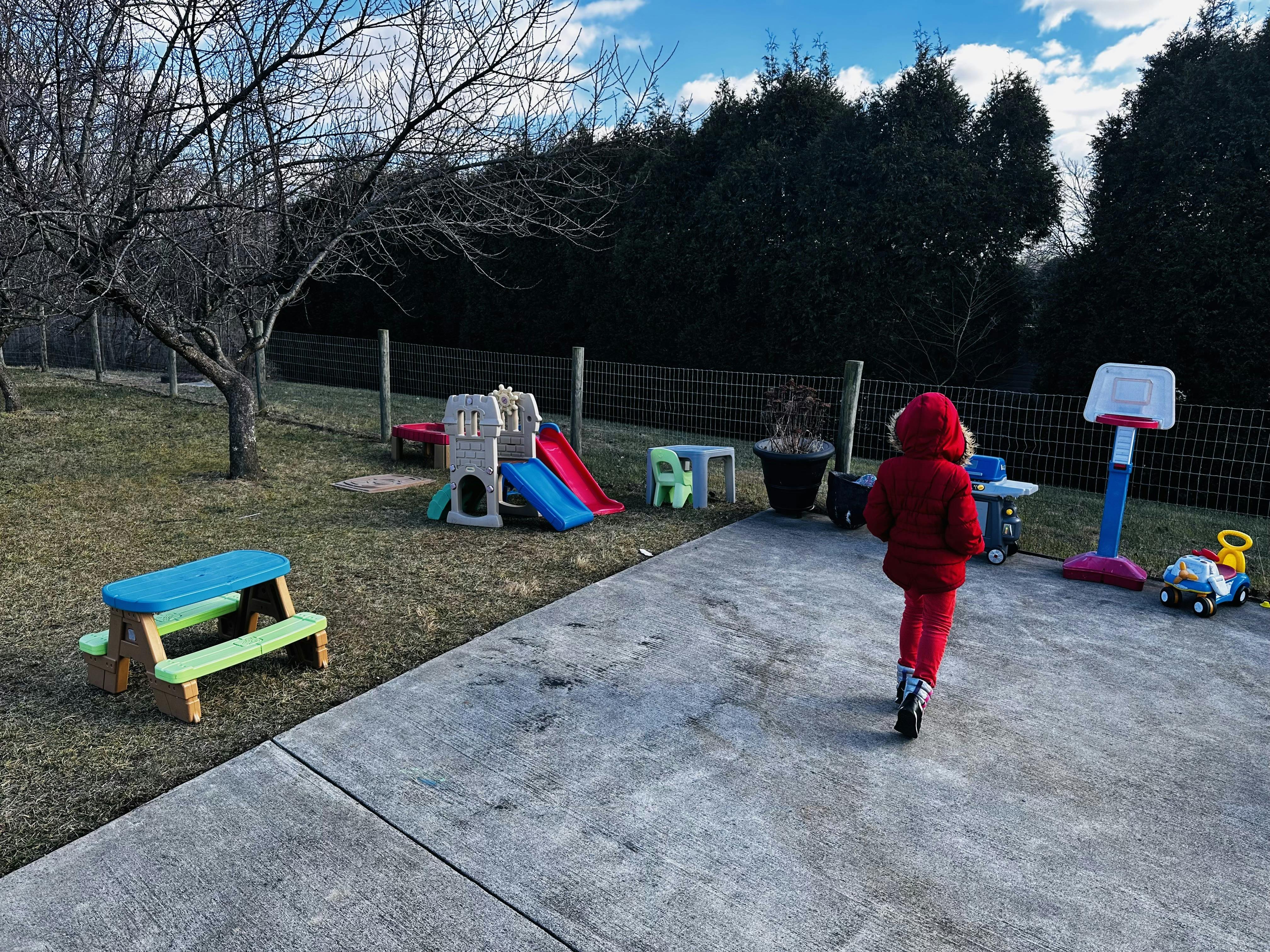 Child in red coat walking on concrete path toward playground equipment