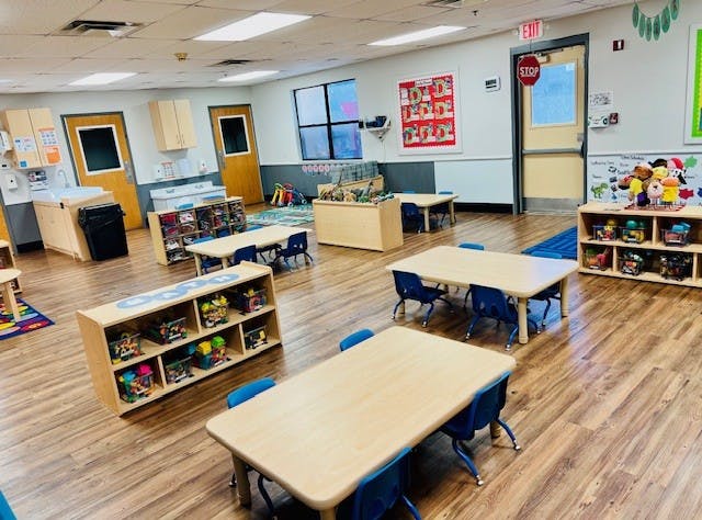 Empty classroom with small tables, blue chairs, and storage shelves
