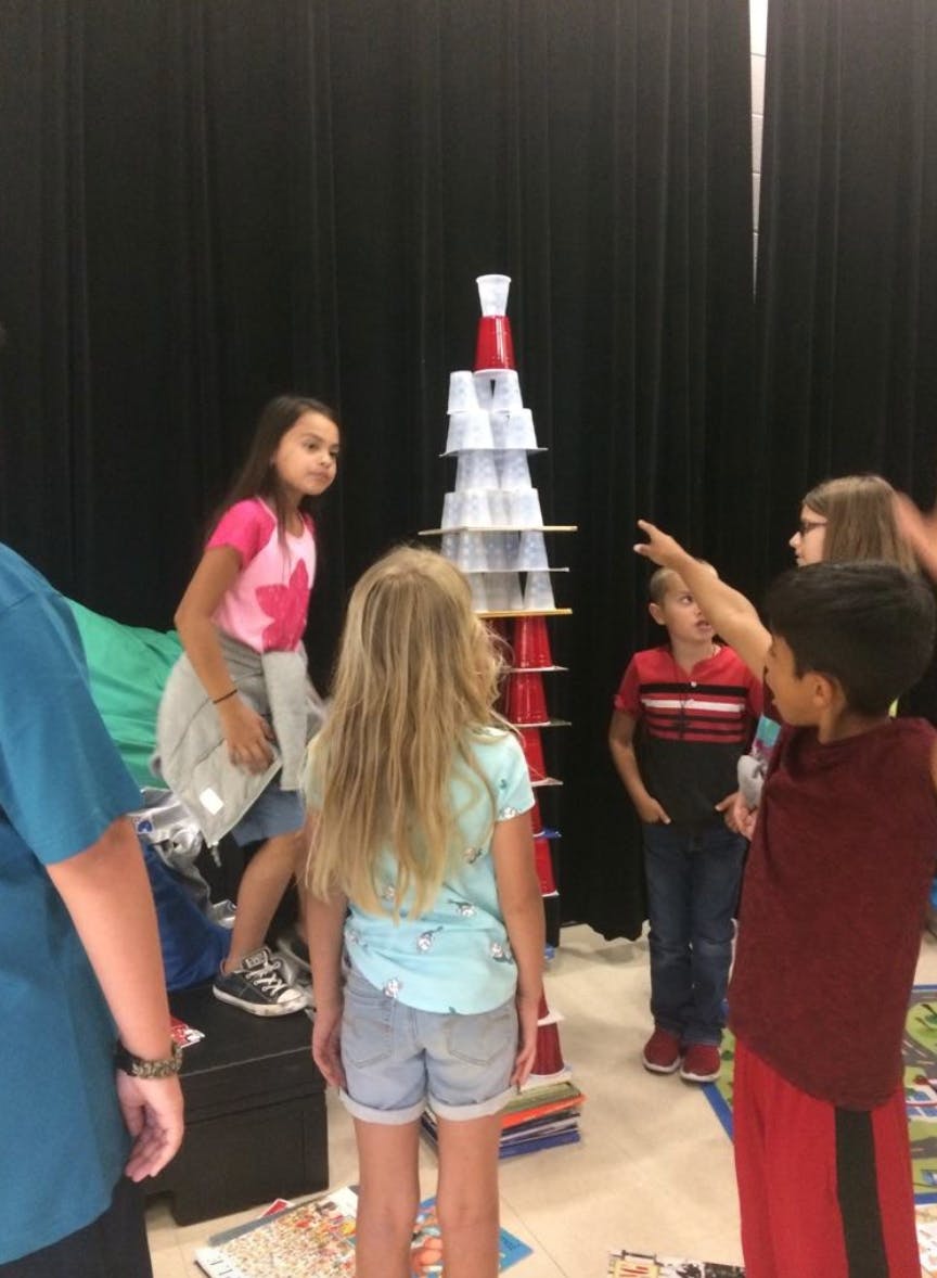 Children gathered around a tall structure made of plastic cups
