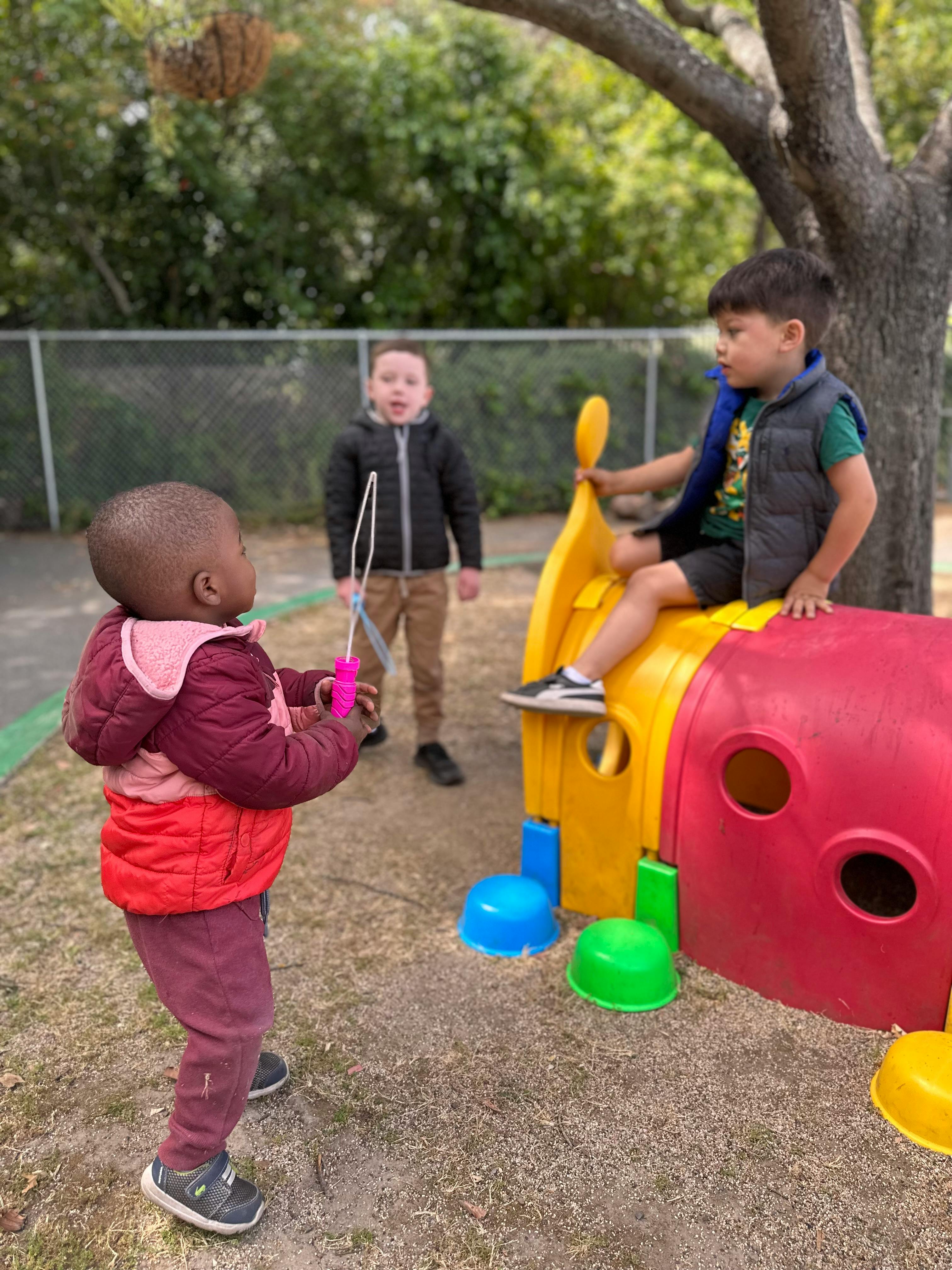 Three children playing outdoors, one holding a bubble wand