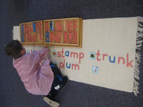 Child arranging letter tiles on a rug to spell words