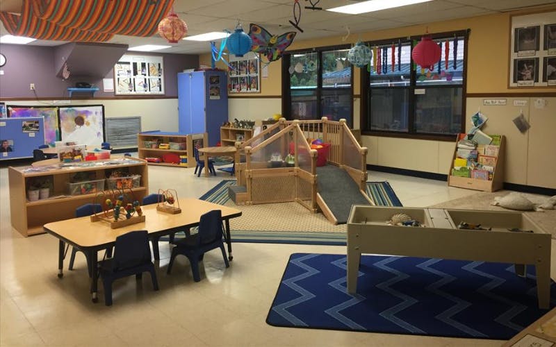 Classroom with child-sized tables, chairs, play structures, and shelves with toys
