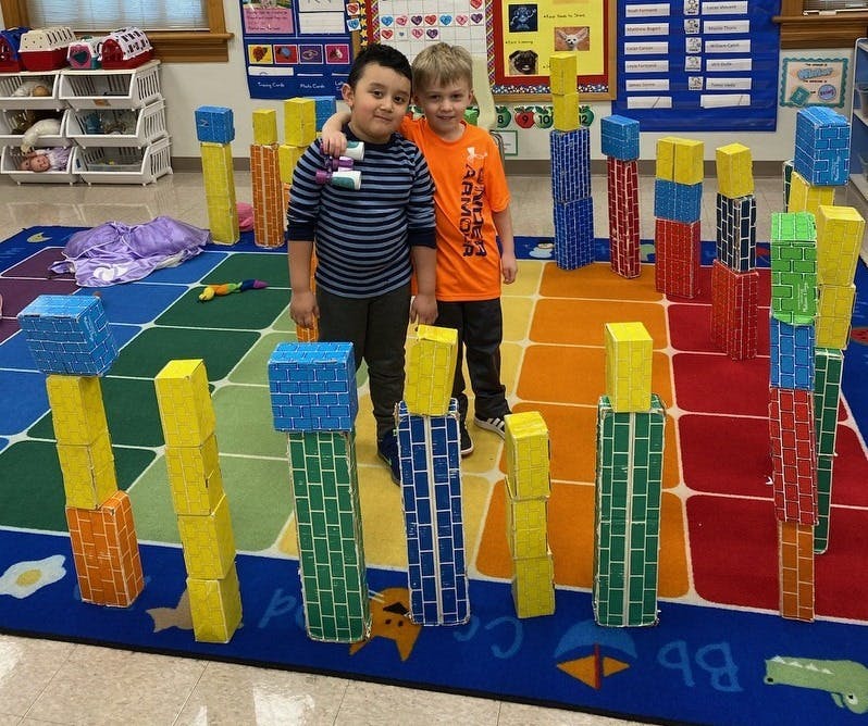 Two children standing among tall block structures in a classroom