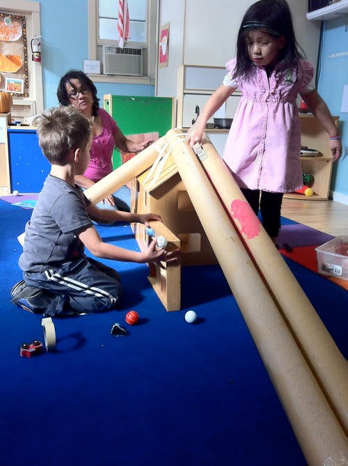 Adult and two children playing with a ball run in a classroom