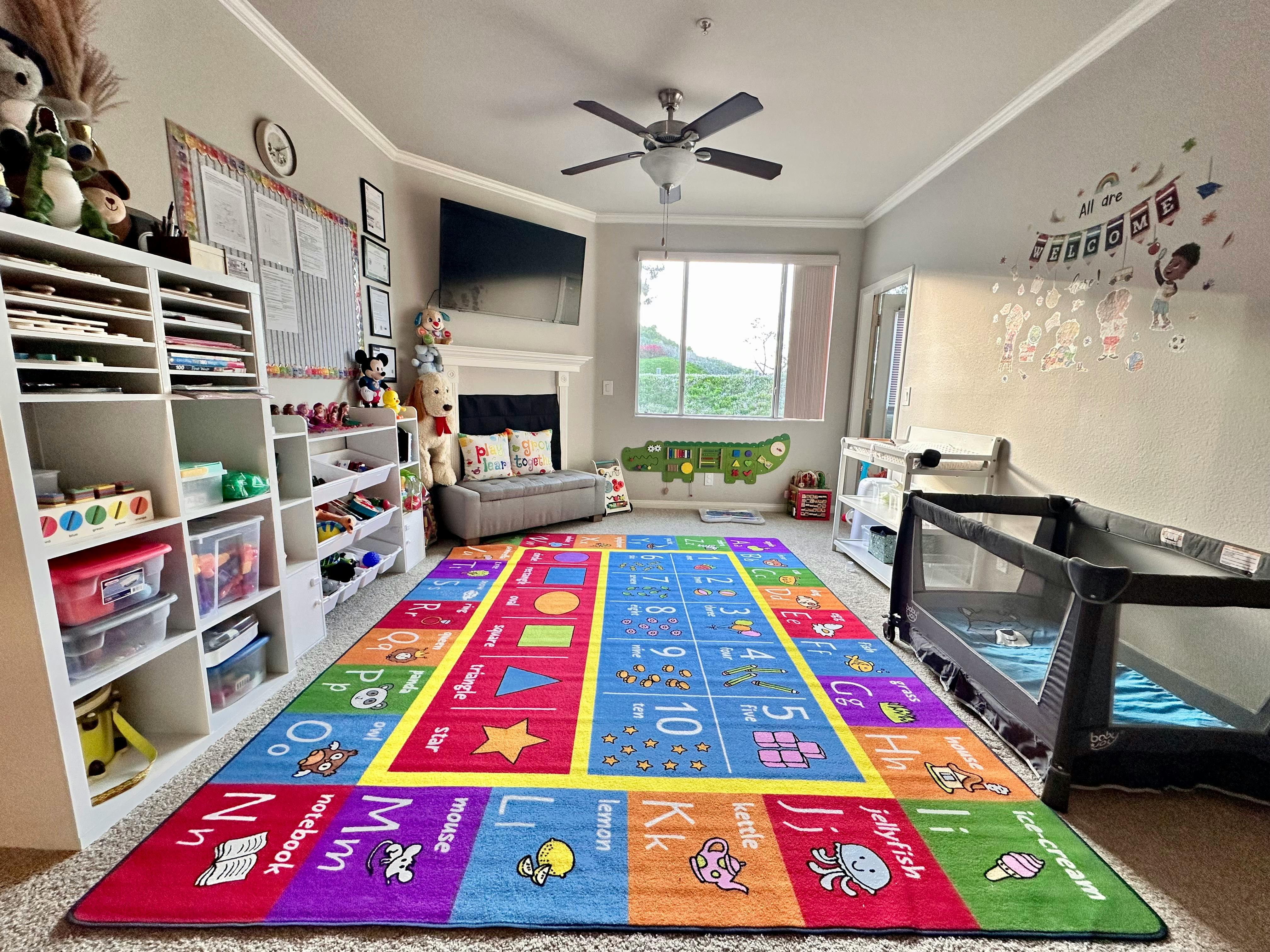 Playroom with colorful alphabet rug, shelves, and two cribs