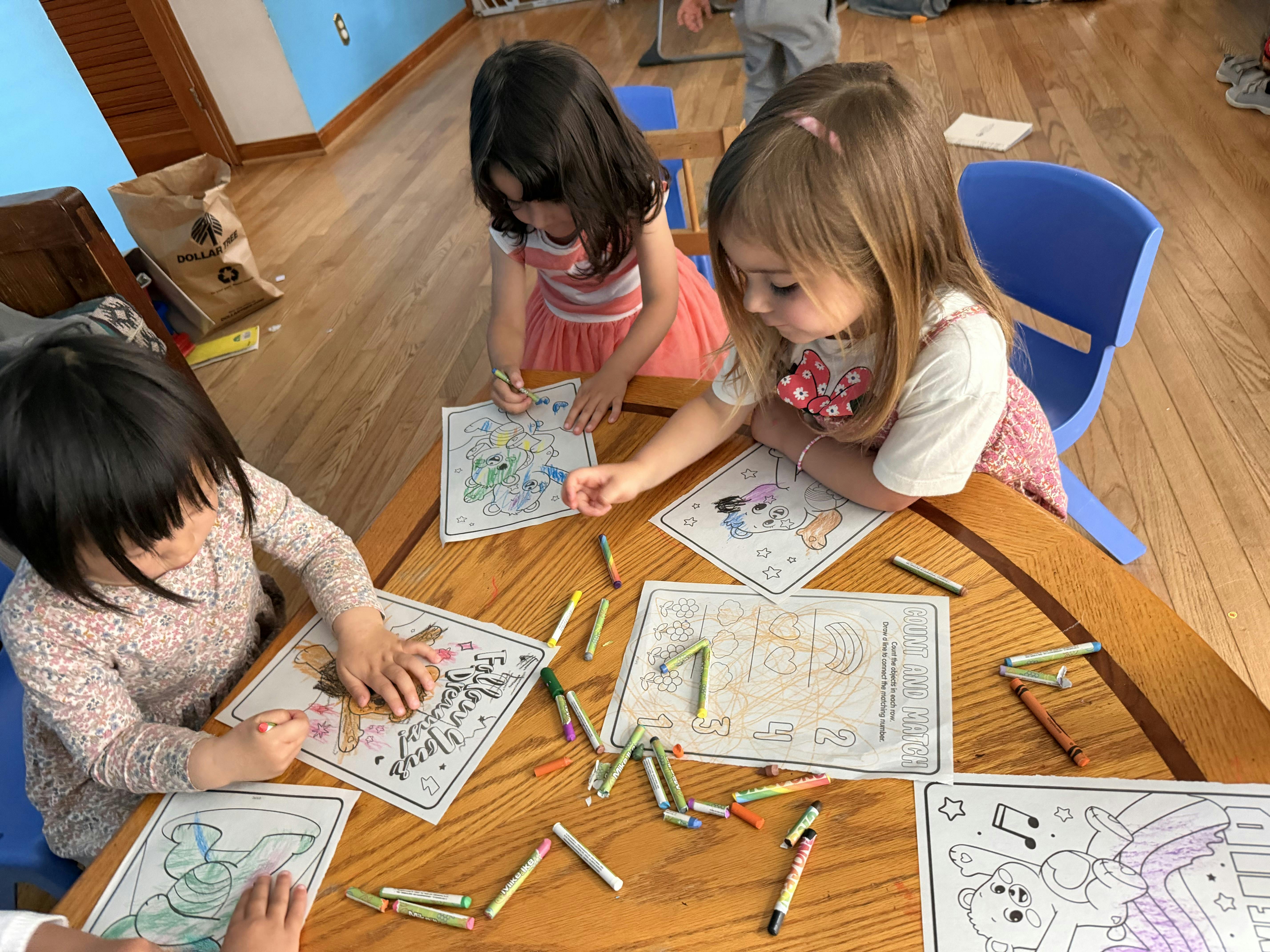 Three children coloring on paper at a round wooden table