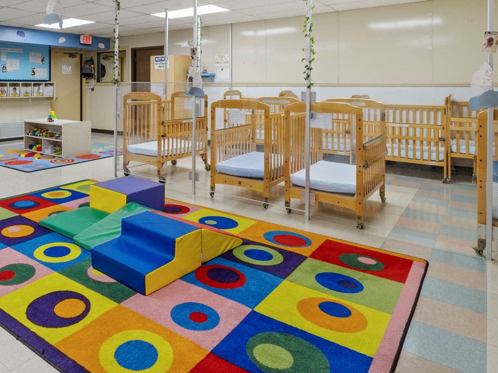 Cribs in a daycare room with a colorful play rug