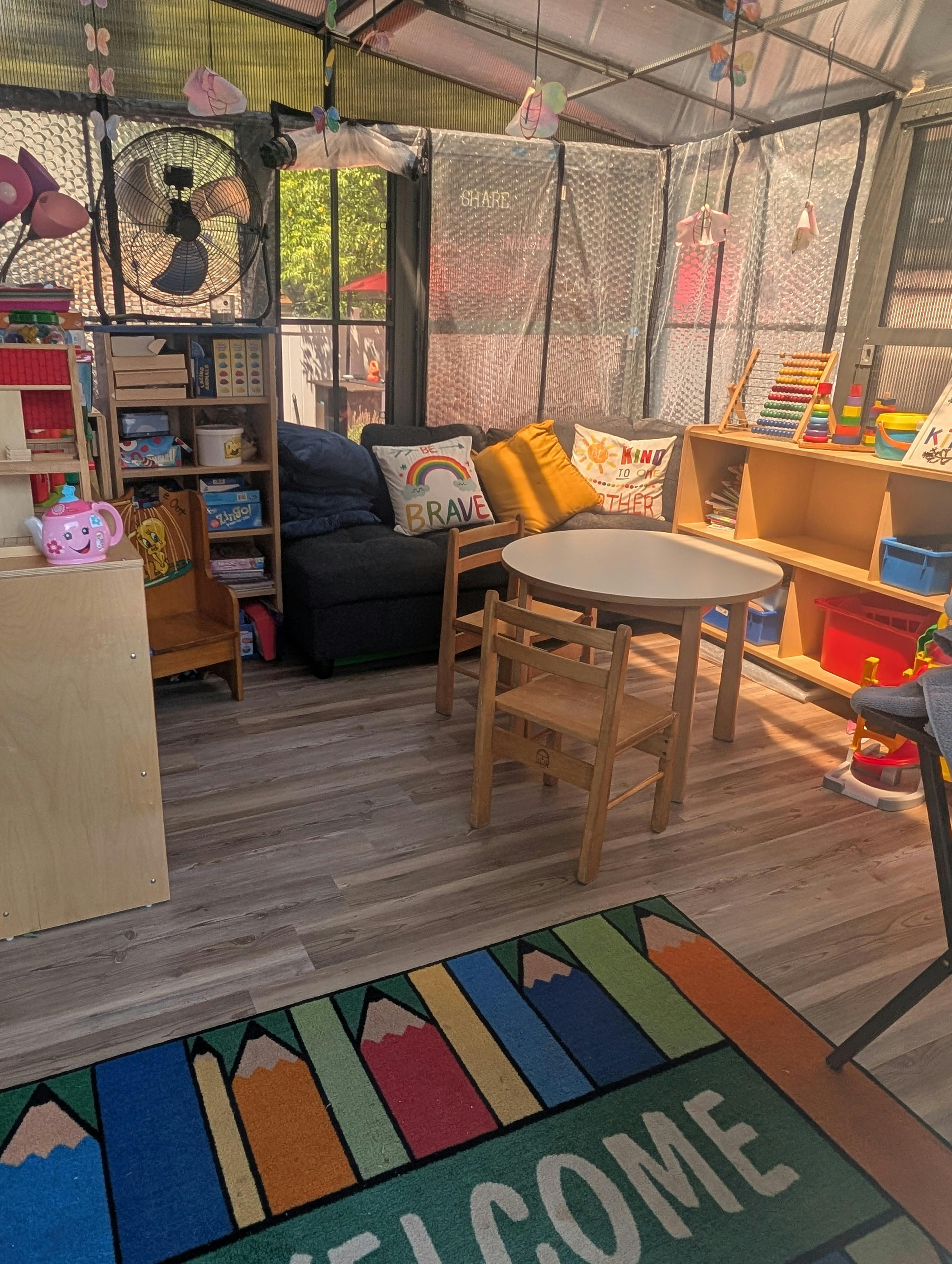 Children's play area with small table and chairs, shelves of toys, and a couch