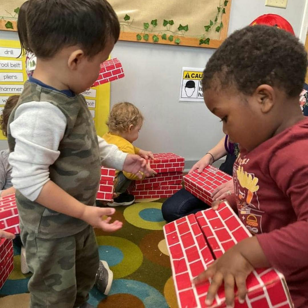 Two children playing with red brick-patterned blocks in a classroom