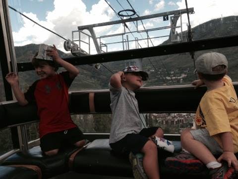 Three children riding in a gondola looking out at the view