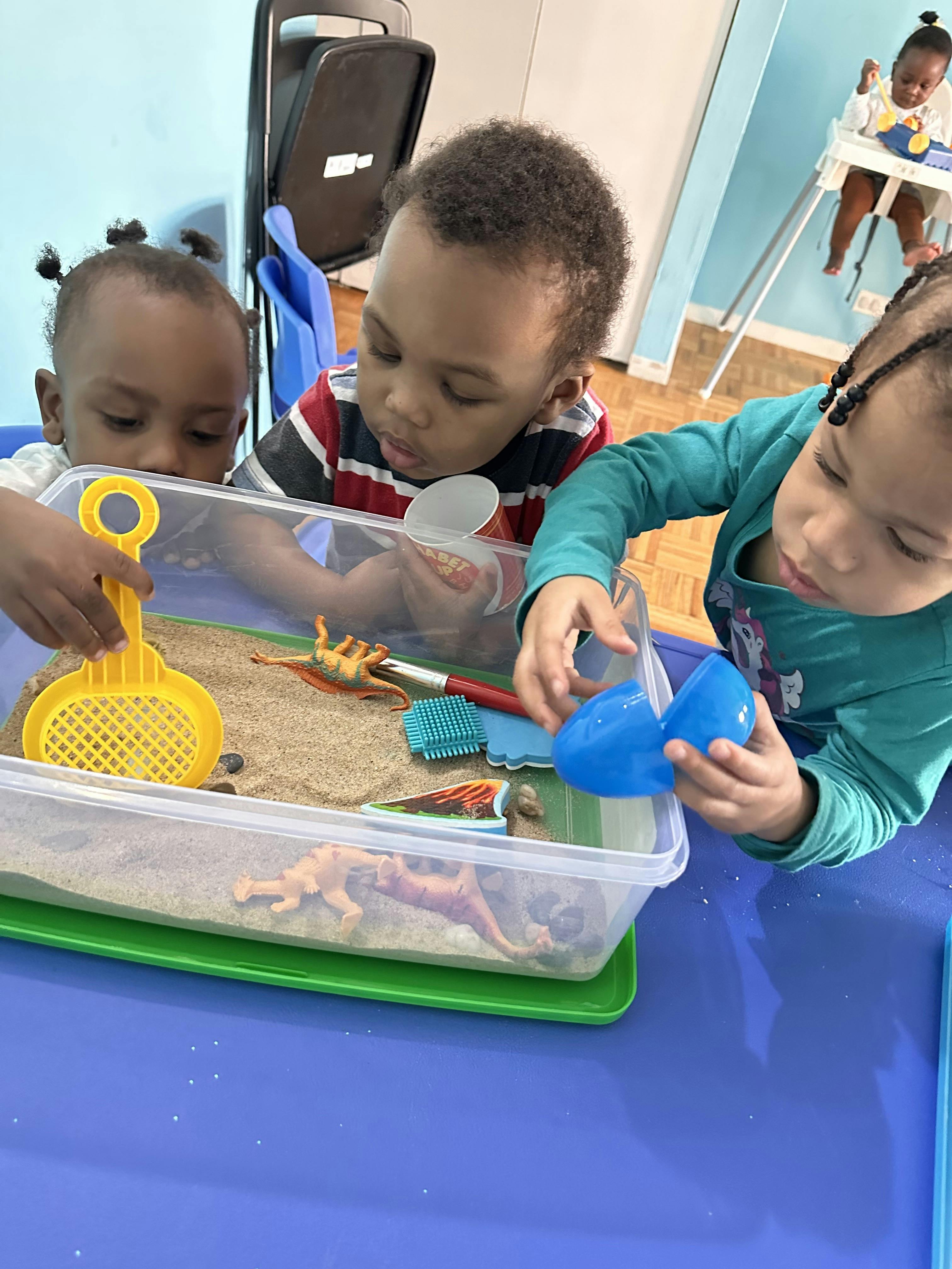 Three children playing with plastic toy dinosaurs in a sandbox