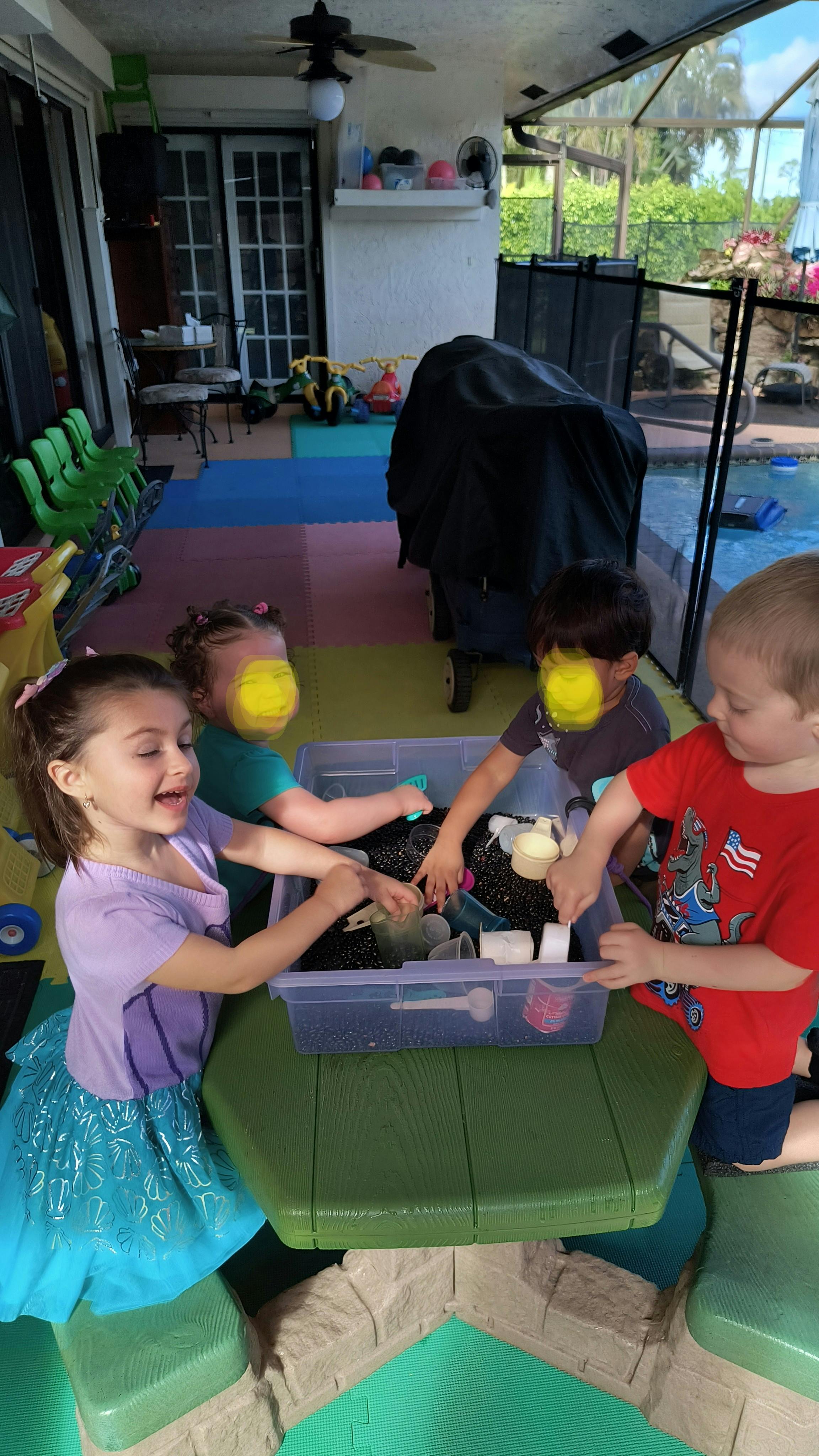 Four children playing with a sensory bin filled with beans at a table
