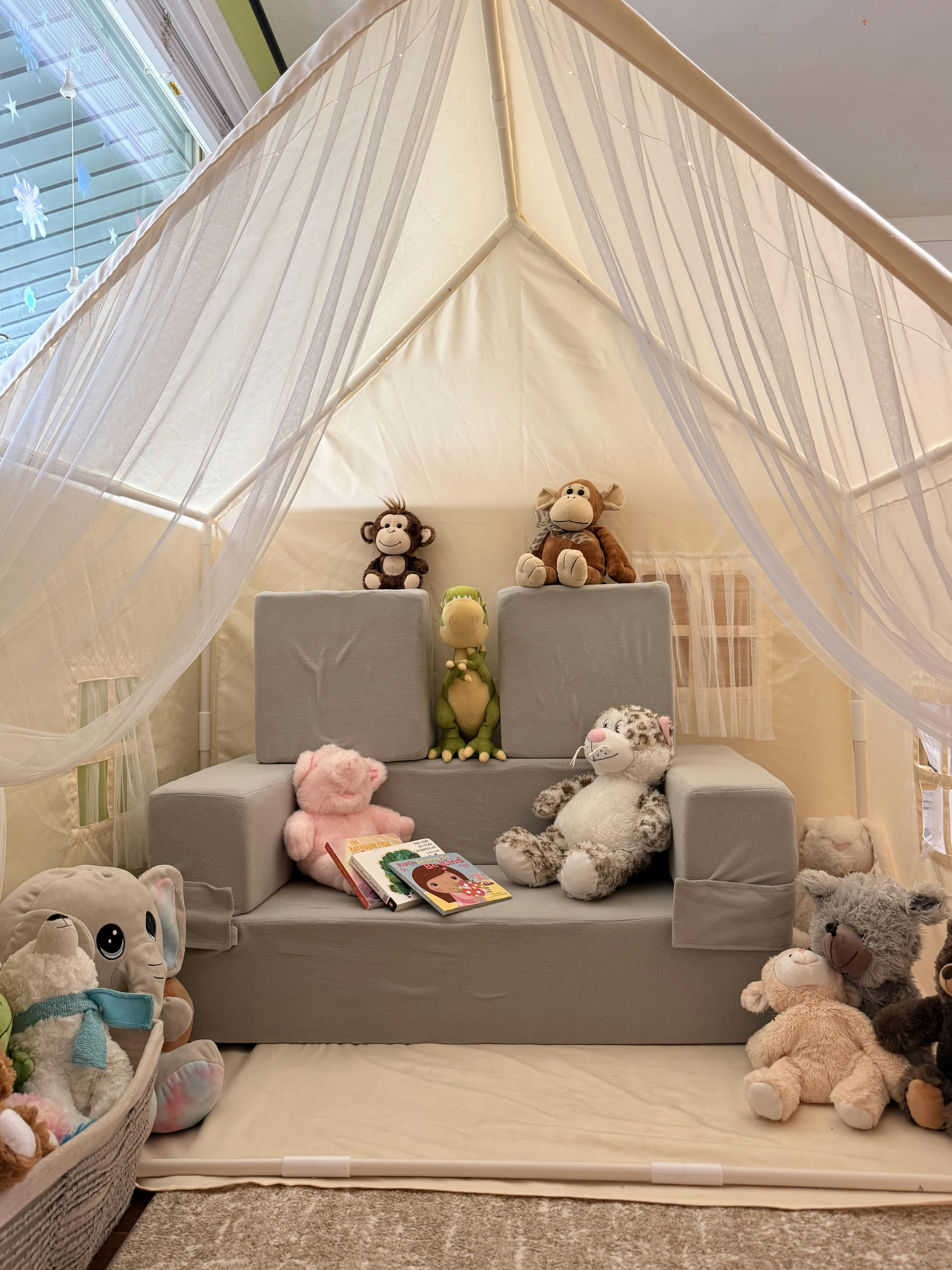 Plush toys and books arranged on a foam couch inside a children's play tent