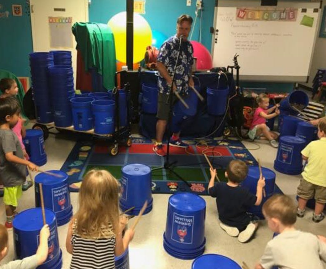 Person playing drums with children playing bucket drums in a classroom