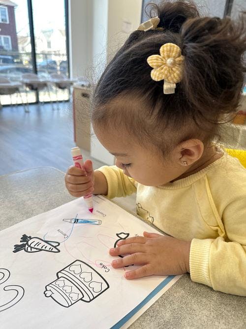 Child coloring a picture of a cake with a pink marker